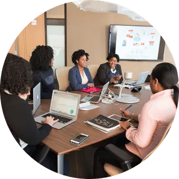 Group of businesswomen in discussion around a meeting table with laptops