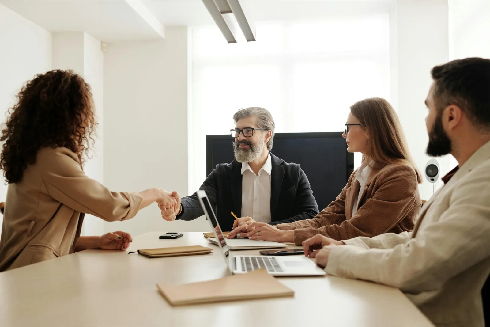 Two people shaking hands across a meeting table while colleagues look on